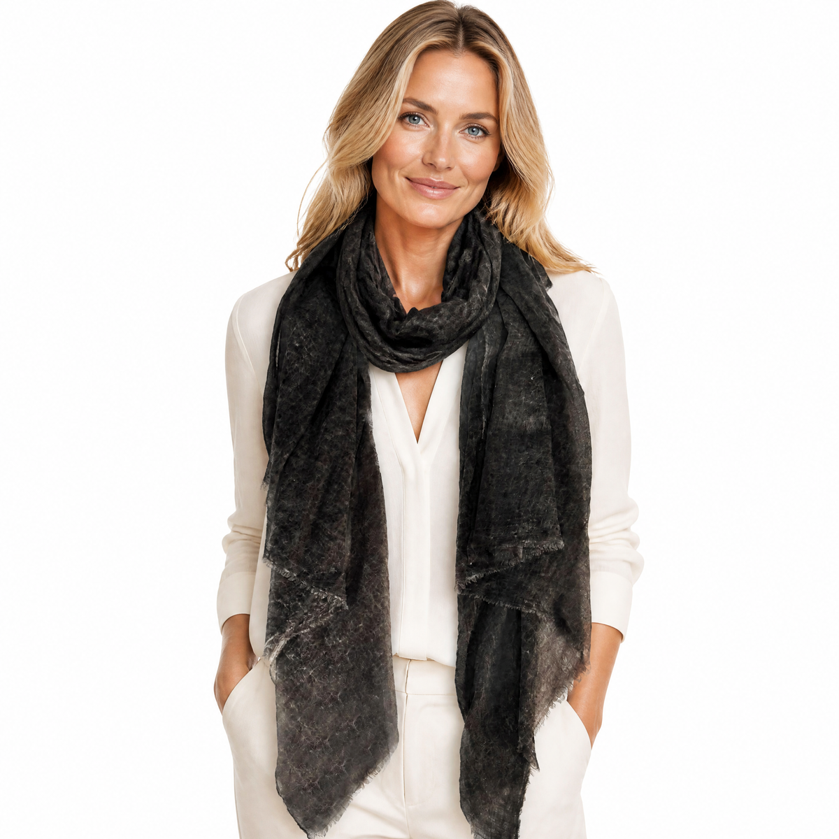 A woman with blonde hair wearing a white blouse and white trousers, styled with a large, lightweight black scarf that has a subtle textured, slightly sheer pattern.